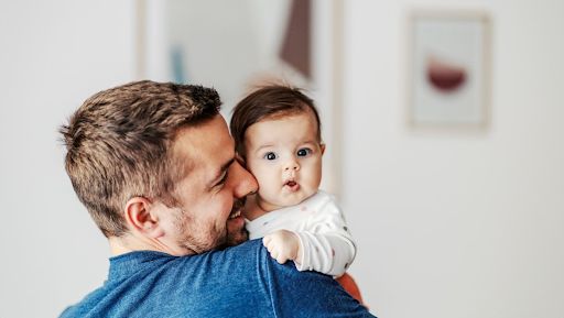 A young father holding his baby who stares into the camera